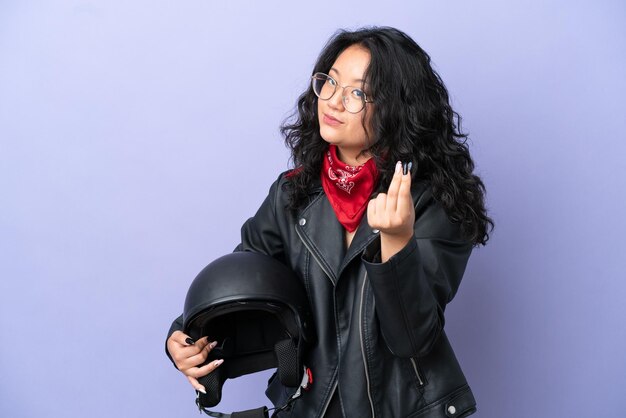 Mujer asiática joven con un casco de motocicleta aislado sobre fondo púrpura haciendo gesto de dinero