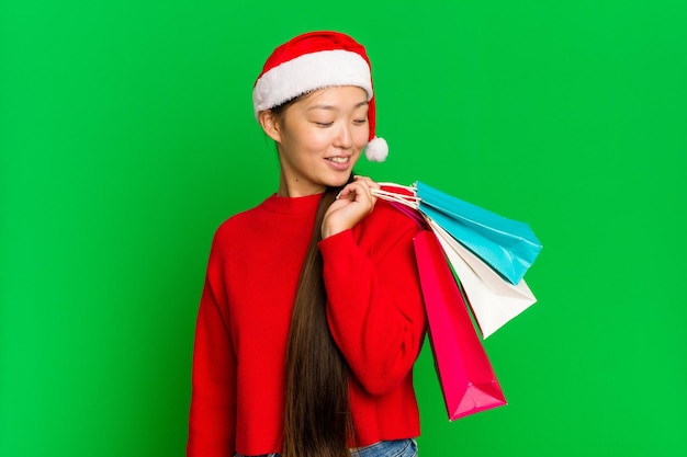 Mujer asiática joven comprando algunos regalos para Navidad aislado sobre fondo de croma verde