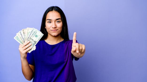 Mujer asiática joven con dinero mostrando el número uno con el dedo.