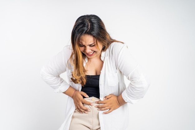 Foto mujer asiática joven en dolor con ambas manos sosteniendo el estómago