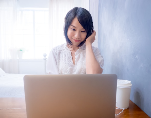 Mujer asiática joven escuchando auriculares delante de la computadora portátil