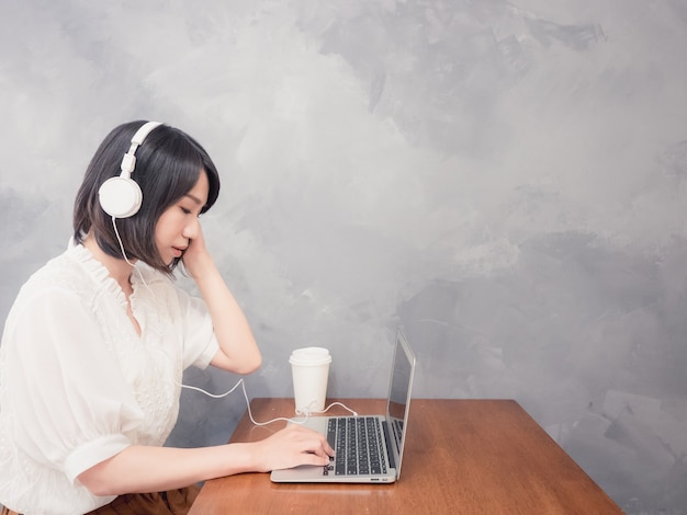 Mujer asiática joven escuchando auriculares delante de la computadora portátil