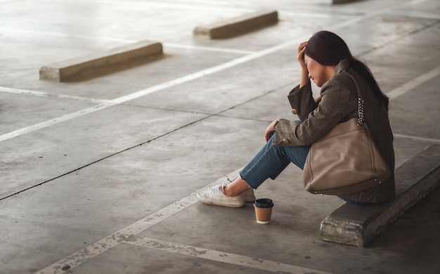 Una mujer asiática joven estresada sentada sola en el estacionamiento