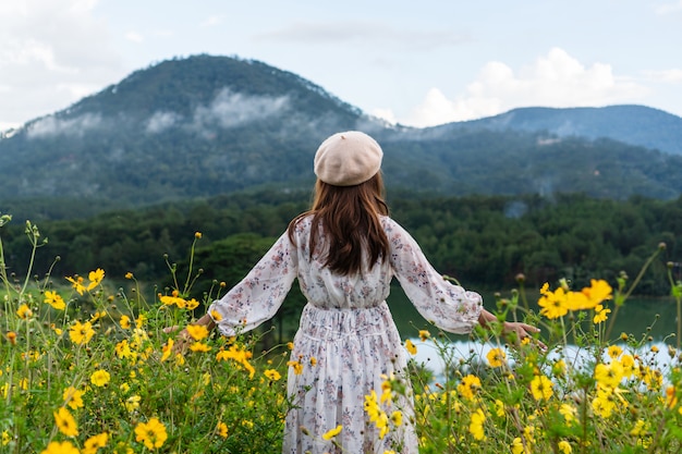 Mujer asiática joven feliz que goza en campo de flor amarilla en la puesta del sol.