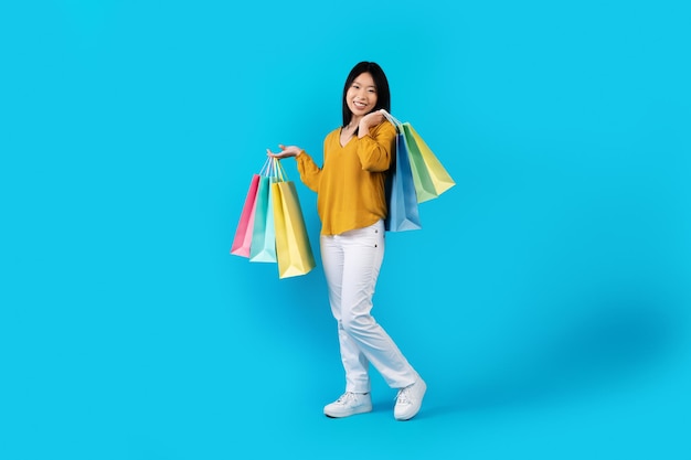 Mujer asiática joven feliz que lleva bolsas de compras coloridas