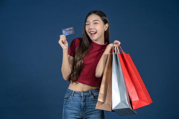 Mujer asiática joven feliz que mira la tarjeta de crédito y que usa el teléfono móvil para las compras en línea