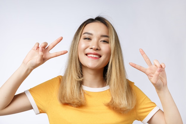 Mujer asiática joven feliz que muestra dos dedos o gesto de la victoria