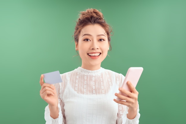 Mujer asiática joven feliz que usa su tarjeta de crédito para hacer compras en línea por su teléfono inteligente.
