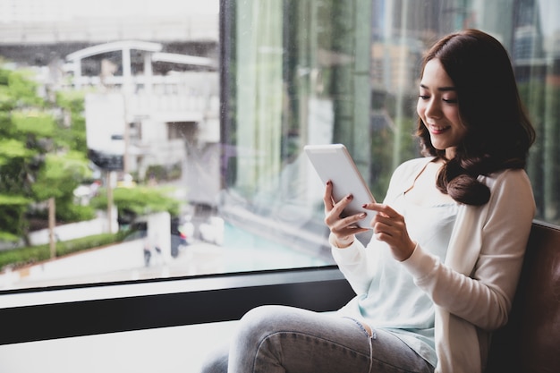 Mujer asiática joven feliz que usa la tableta digital y siente felicidad mientras lee un libro electrónico, una biblioteca de medios o estudia un concepto en línea de E-learning