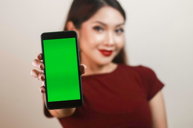 Mujer asiática joven feliz y sonriente que muestra y que señala a una pantalla en blanco verde