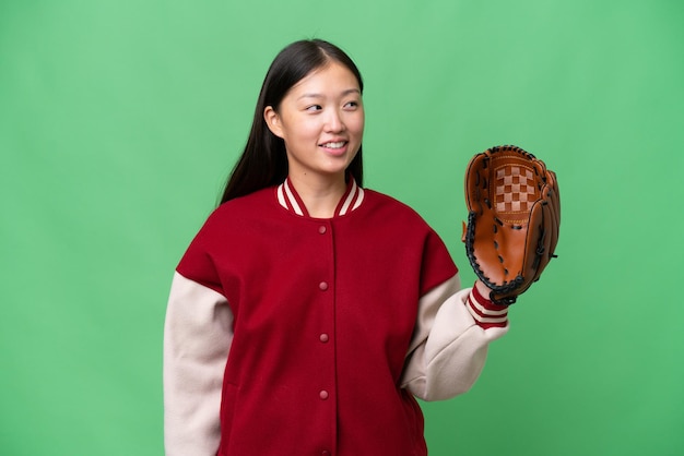 Mujer asiática joven con guante de béisbol sobre fondo aislado mirando hacia el lado