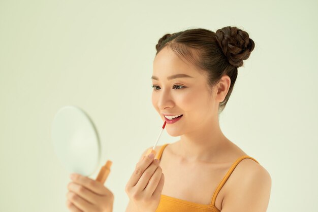 Mujer asiática joven hermosa que aplica el lápiz labial sobre fondo claro.