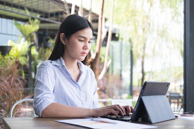 La mujer asiática joven independiente está trabajando con la tableta en la cafetería Trabajando en línea