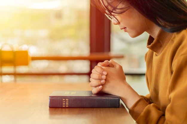 Mujer asiática joven con las manos dobladas en oración sobre una Biblia sagrada