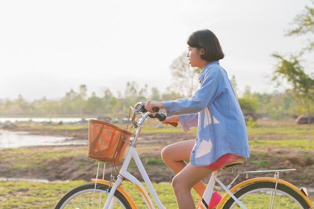 Mujer asiática joven montando bicicleta en el parque con puesta de sol