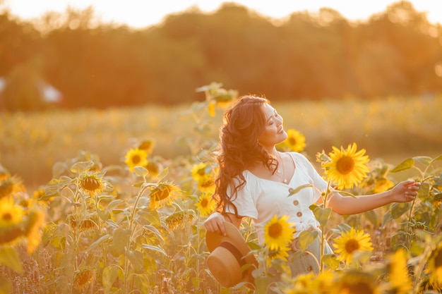 Mujer asiática joven con el pelo rizado en un campo de girasoles al atardecer.