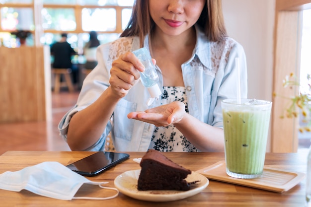 Mujer asiática joven que aplica desinfectante de manos para limpiar su mano antes de comer. Concepto de salud.