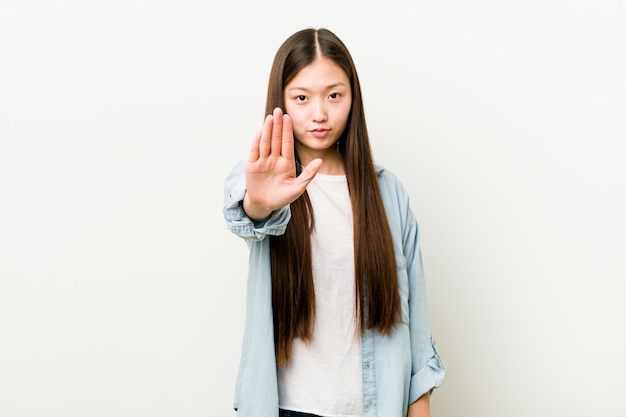 Mujer asiática joven que se coloca con la mano extendida que muestra la señal de stop, previniéndole.