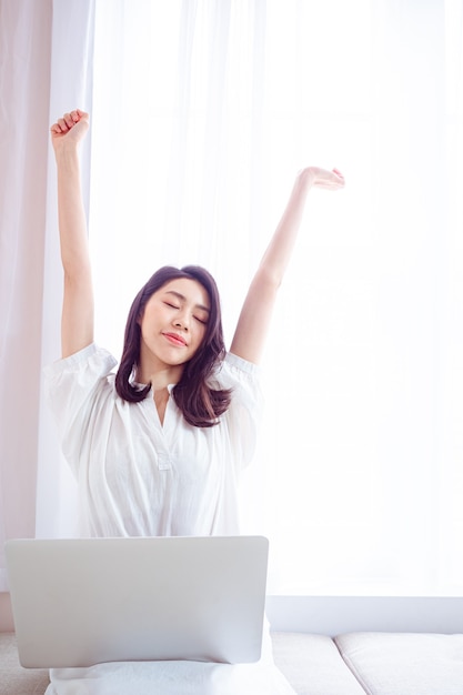 Mujer asiática joven que estira sus brazos después de usar la computadora portátil.