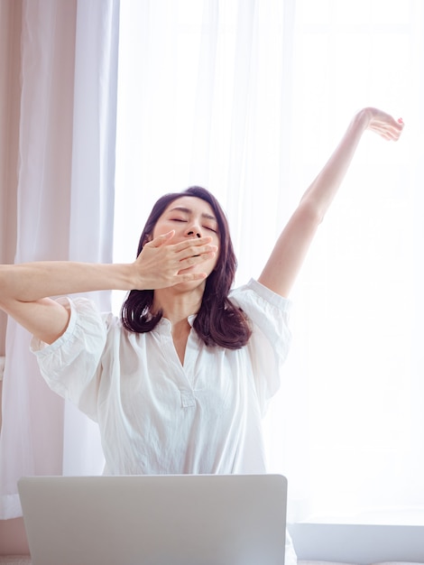 Mujer asiática joven que estira sus brazos después de usar la computadora portátil.