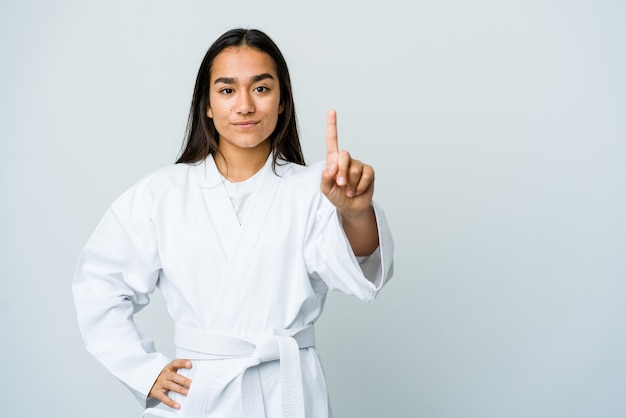 Mujer asiática joven que hace karate aislado en blanco que muestra el número uno con el dedo.