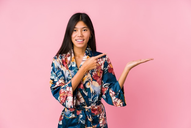 La mujer asiática joven que llevaba un pijama del kimono excitó sostener un espacio de la copia en la palma.