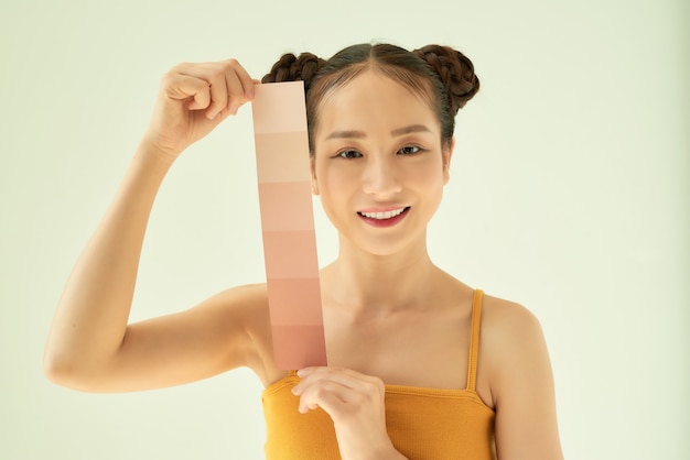 Mujer asiática joven que muestra la paleta de tonos de piel mientras está de pie aislado sobre fondo claro.