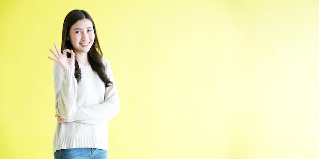 Mujer asiática joven que muestra el signo de la mano ok mientras está de pie sobre un fondo amarillo aislado