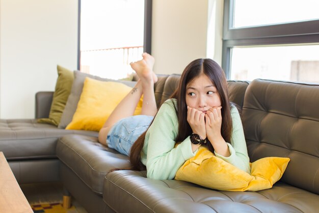 Mujer asiática joven que parece preocupada, ansiosa, estresada y asustada, mordiéndose las uñas y mirando al espacio de copia lateral