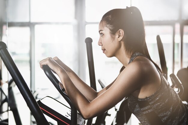 Mujer asiática joven que se resuelve en una máquina de ejercicio en el gimnasio moderno