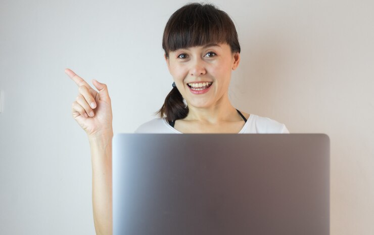 Mujer asiática joven que sonríe y que señala el dedo con la computadora portátil.