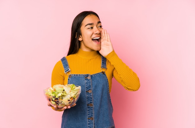 La mujer asiática joven que sostenía una ensalada aisló gritar y sostener la palma cerca de boca abierta.