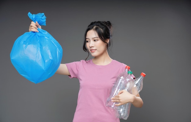 Mujer asiática joven que sostiene la bolsa de basura en el fondo