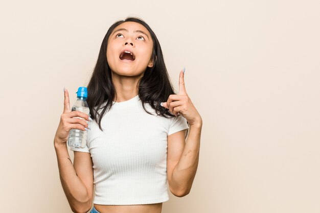 Mujer asiática joven que sostiene una botella de agua apuntando al revés con la boca abierta.