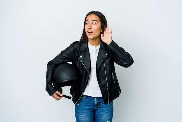 Mujer asiática joven que sostiene un casco de moto tratando de escuchar un chisme.