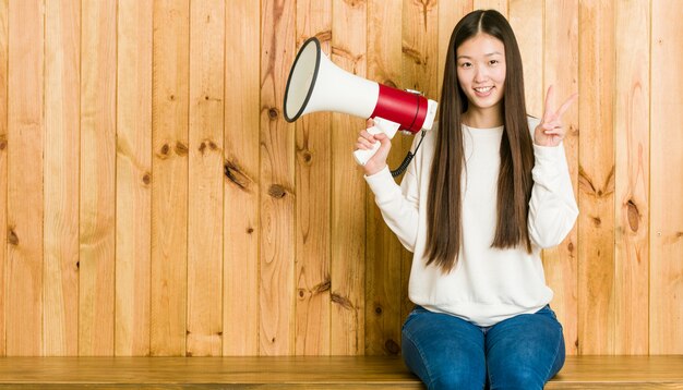 Mujer asiática joven que sostiene un megáfono que muestra el número dos con los dedos.