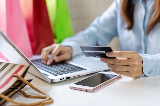 Foto mujer asiática joven que sostiene una tarjeta de crédito y usa una computadora portátil para hacer un pago de compras en línea en casa