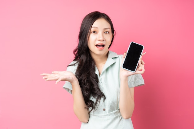 Mujer asiática joven que sostiene el teléfono en la mano con mirada sorprendida en rosa