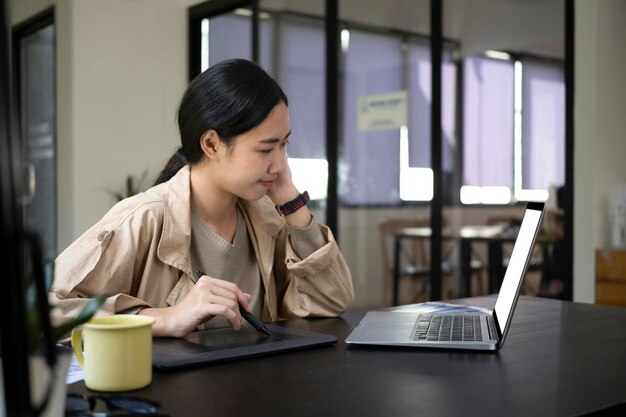 Mujer asiática joven que trabaja con tableta gráfica en la oficina creativa