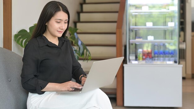 Mujer asiática joven que usa una computadora portátil en una cafetería comprando en línea o chateando en línea en las redes sociales