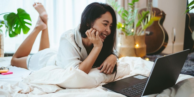 Mujer asiática joven que usa una computadora portátil para hacer negocios en línea, trabajo independiente femenino que trabaja desde casa usando la tecnología de comunicación del ciberespacio de Internet para el trabajo de una mujer de negocios