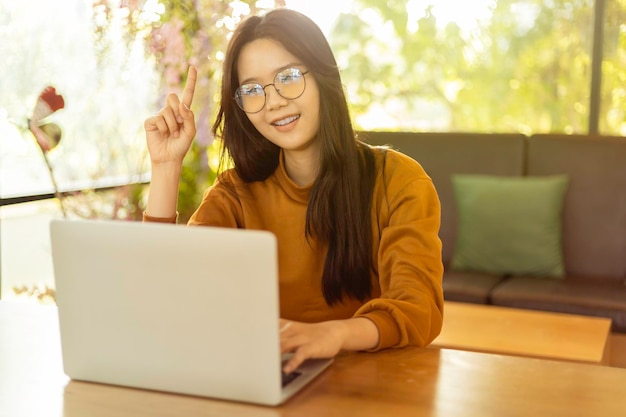 Mujer asiática joven que usa una computadora portátil y señala con el dedo hacia arriba con la luz del sol de la mañana