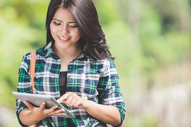 Mujer asiática joven que usa una PC de la tableta mientras camina en el parque