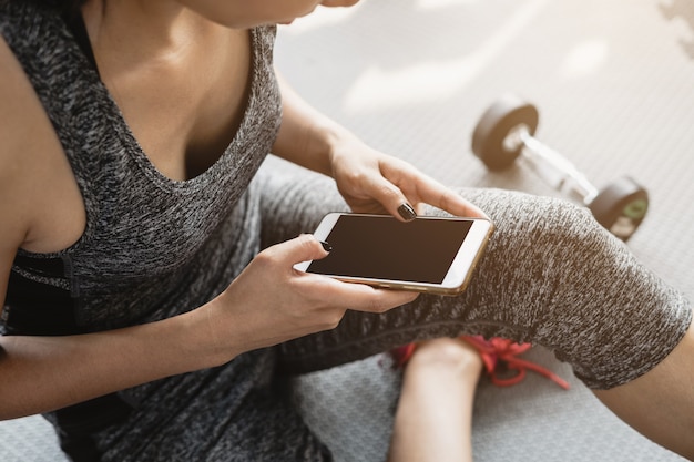 Mujer asiática joven que usa smartphone en gimnasio