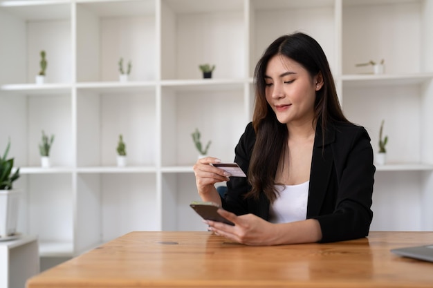 Mujer asiática joven que usa tarjeta de crédito y teléfono móvil para comprar en línea en una cafetería o espacio de coworking tecnología de taza de café billetera de dinero y maqueta de tarjeta de crédito de concepto de pago en línea