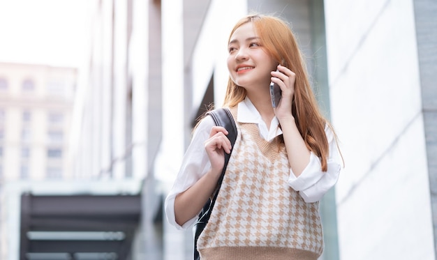 Mujer asiática joven que usa el teléfono inteligente en la calle