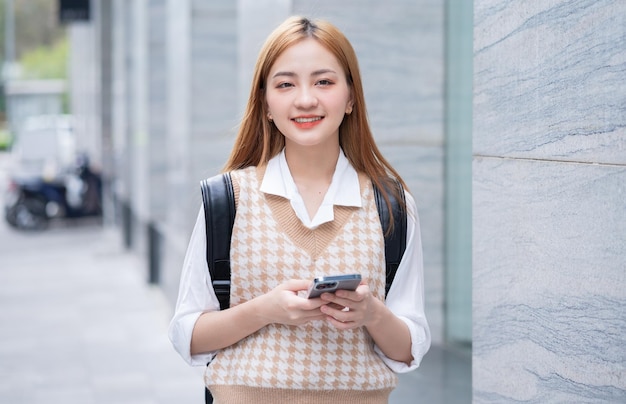 Mujer asiática joven que usa el teléfono inteligente en la calle