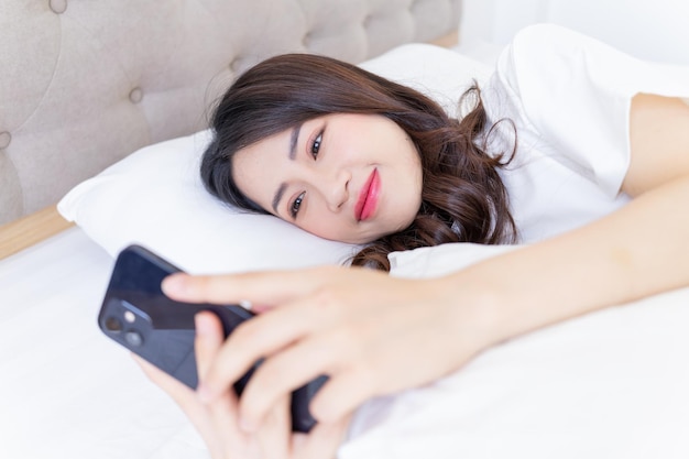 Mujer asiática joven que usa el teléfono inteligente en la cama