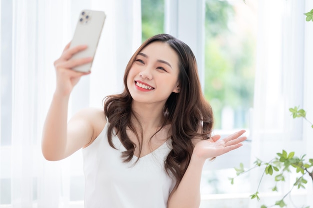Mujer asiática joven que usa el teléfono inteligente en casa por la mañana