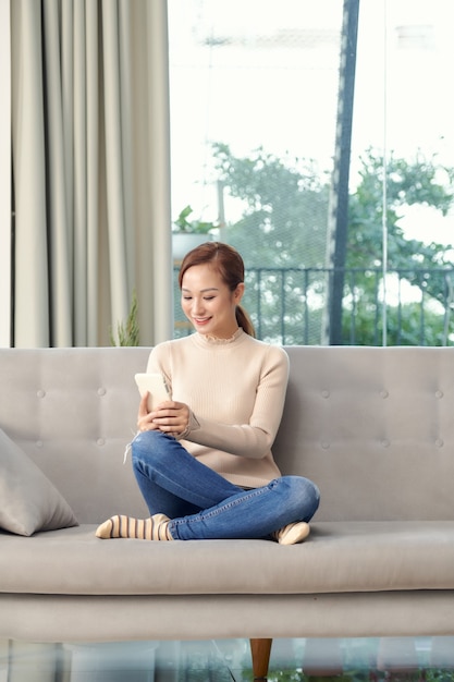 Mujer asiática joven que usa un teléfono inteligente en la habitación.